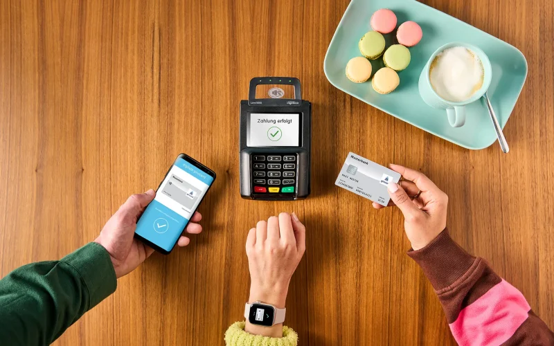 Payment transaction with smartphone and credit card at a modern card reader, surrounded by a cup of coffee and colorful macarons on a tray.